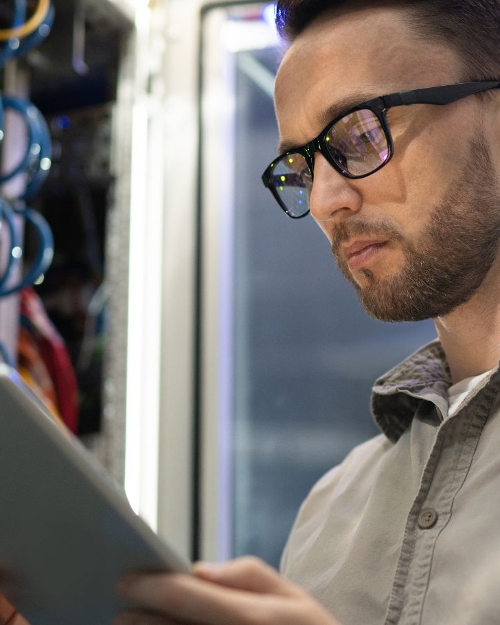 Man wearing glasses works on his tablet in a server room