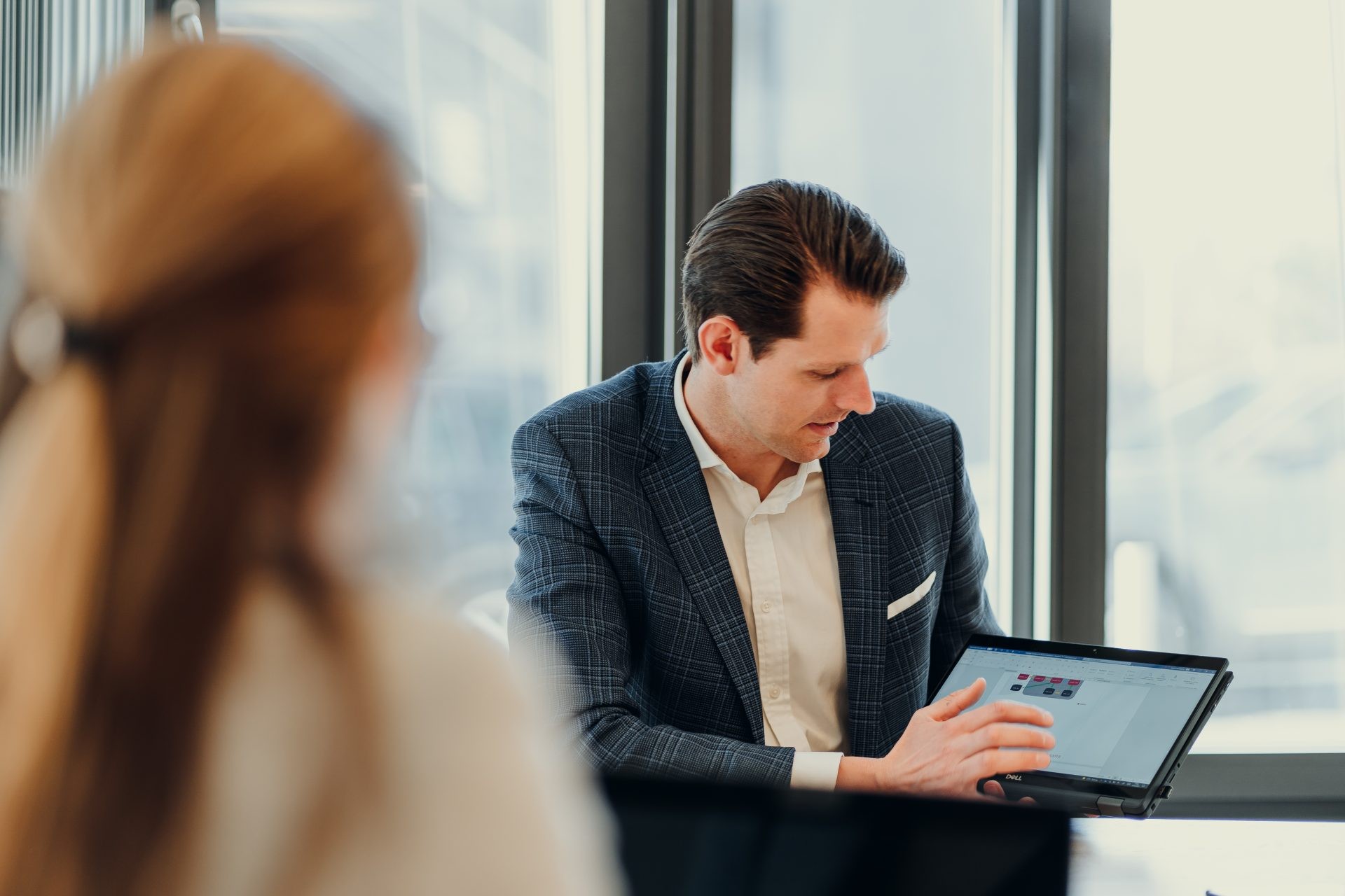 Ein Geschäftsmann im Anzug erklärt einer Gesprächspartnerin etwas und zeigt dabei auf eine Grafik auf seinem Laptop-Bildschirm