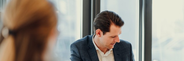 Ein Geschäftsmann im Anzug erklärt einer Gesprächspartnerin etwas und zeigt dabei auf eine Grafik auf seinem Laptop-Bildschirm