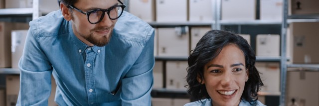 male and female co-workers chat over a laptop in a warehouse
