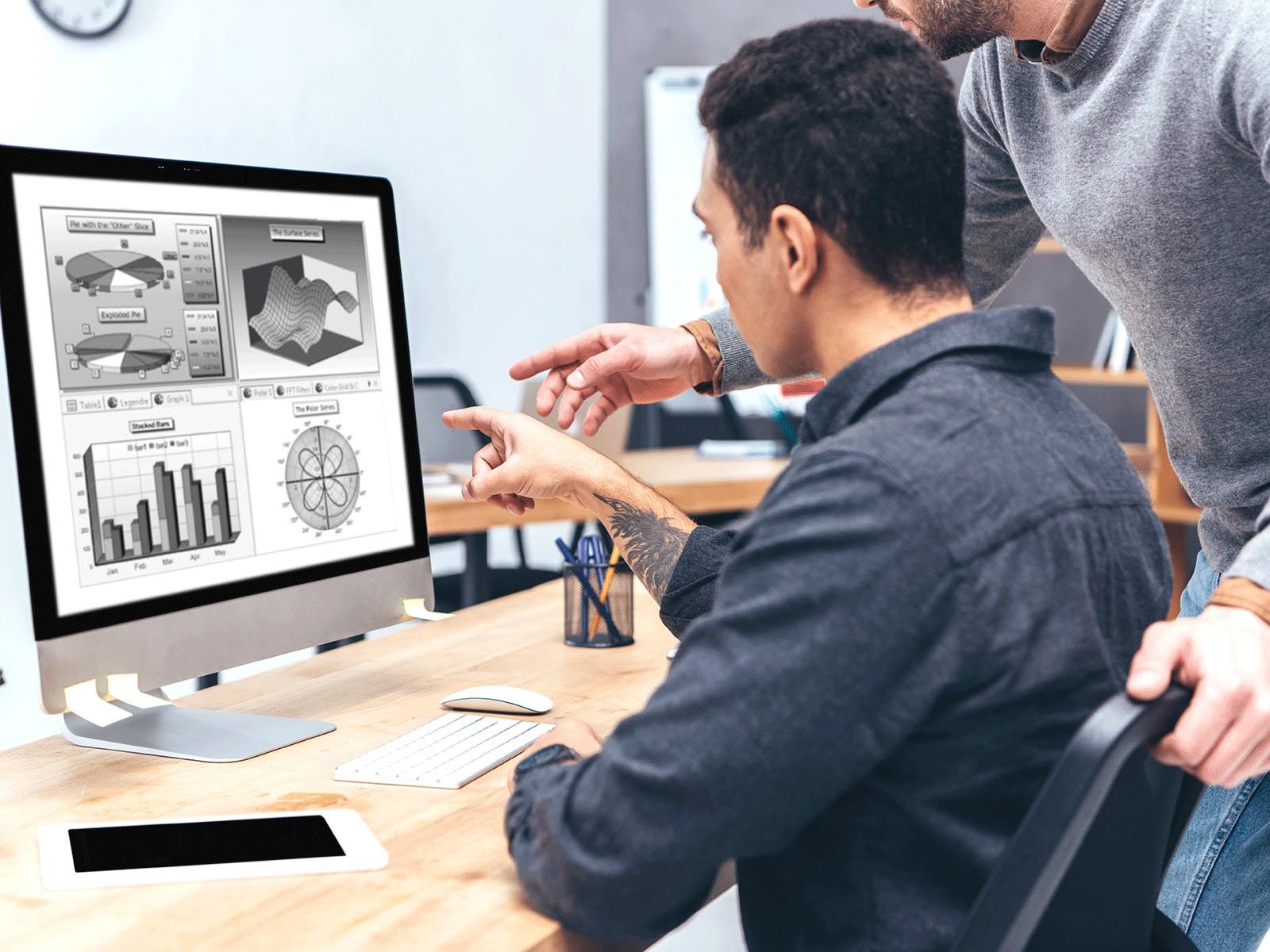 A man helping another man analyze data and business information on a computer