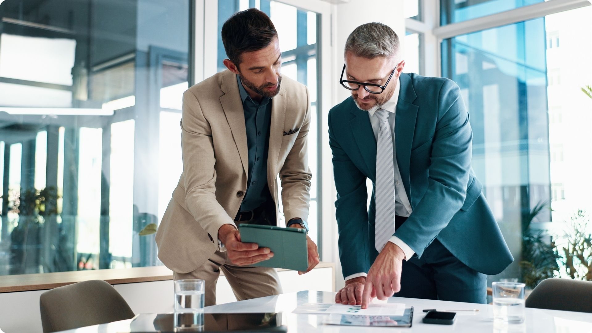 Two men in suits confer over a digital tablet