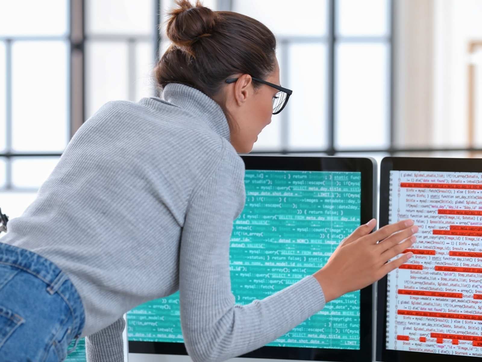 Woman examining data and code on two computers