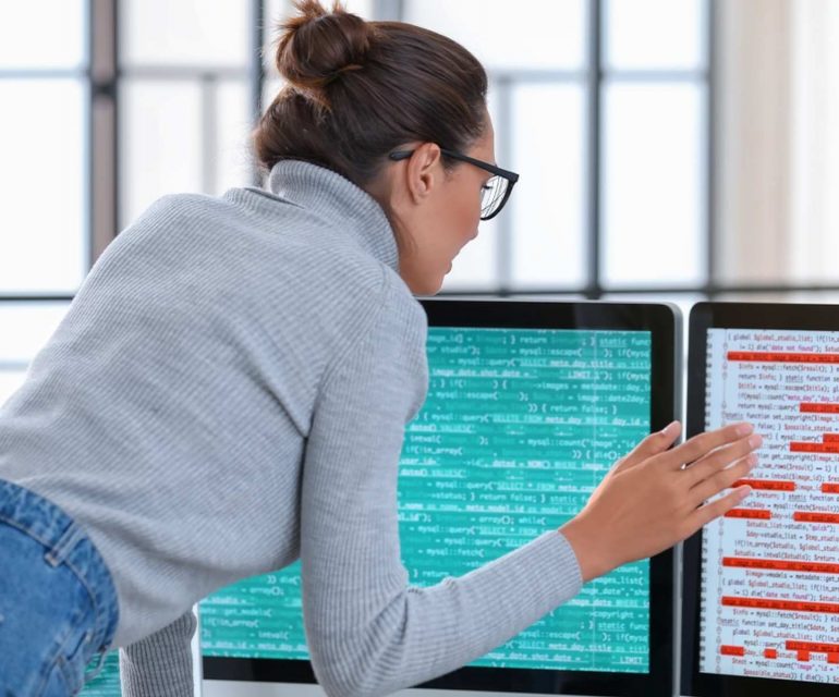 Woman examining data and code on two computers